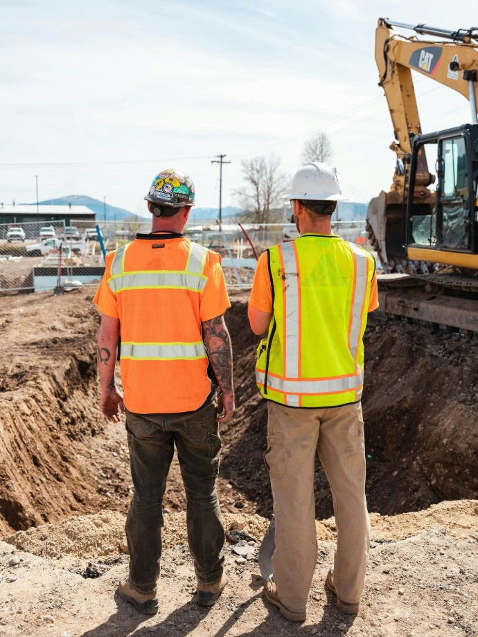Hombres con chalecos de seguridad de pie frente a un vehículo de construcción